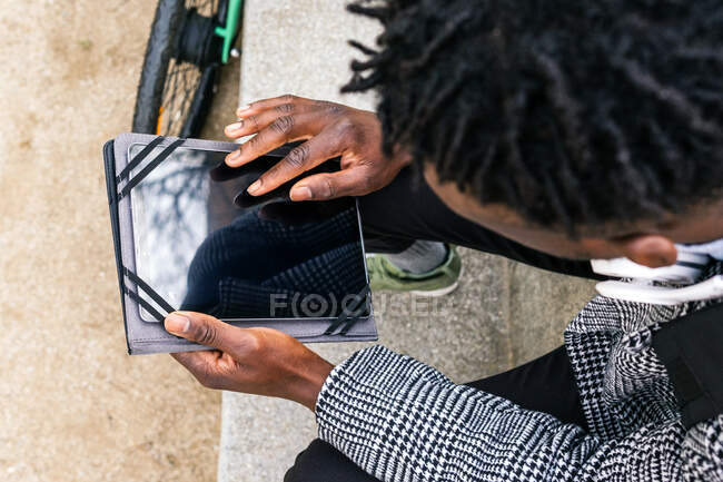 Vista superior de los jóvenes contentos afroamericanos gerente masculino con la tableta y auriculares mirando hacia otro lado contra el edificio urbano - foto de stock