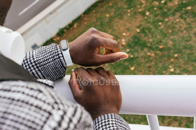 Crop anonymous ethnic male entrepreneur watching time on modern wearable bracelet on fenced bridge in city — Stock Photo