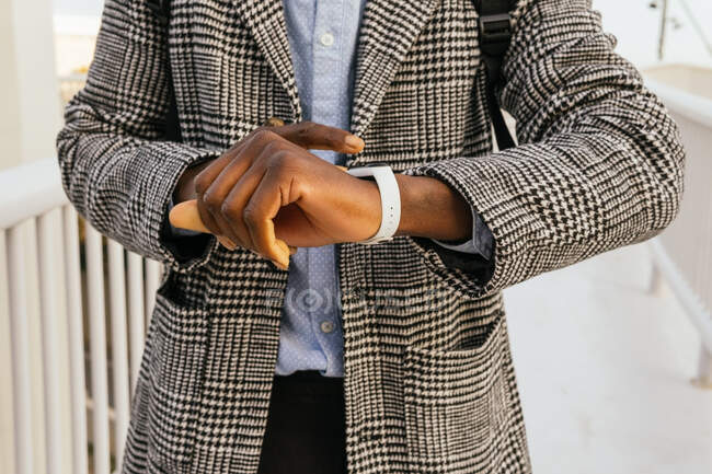 Ernte anonyme ethnische männliche Unternehmer beobachten die Zeit auf modernen tragbaren Armband auf eingezäunten Brücke in der Stadt — Stockfoto