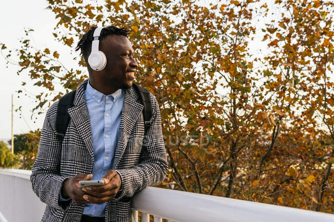 Side view of content African American male manager in headset text messaging on cellphone near fence in town — Stock Photo