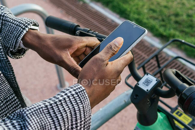 Dall'alto del raccolto anonimo etnico maschile impiegato utilizzando l'applicazione sul cellulare con schermo nero durante il parcheggio della bicicletta in città — Foto stock