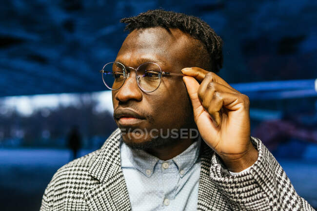 Молодий афроамериканець, який працює офісним працівником в афроамериканській конторі, торкається окулярів, дивлячись у місто на сутінках. — стокове фото
