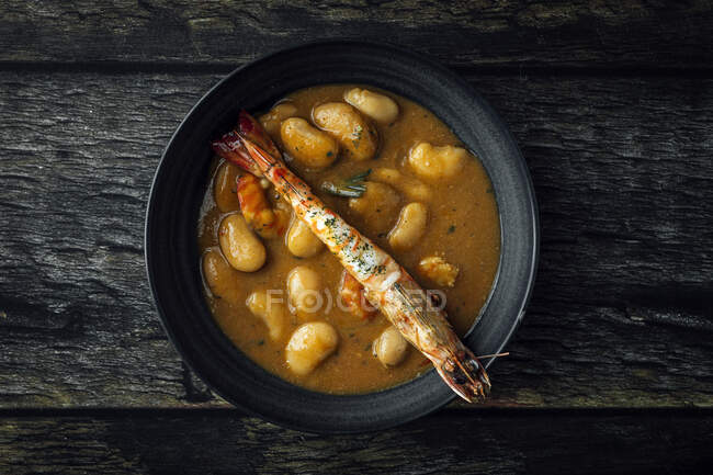 From above of appetizing cream soup with white beans and langoustines served in bowl and placed on wooden tabletop in kitchen — Stock Photo