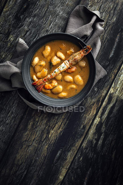 From above of appetizing cream soup with white beans and langoustines served in bowl and placed on wooden tabletop near napkin in kitchen — Stock Photo