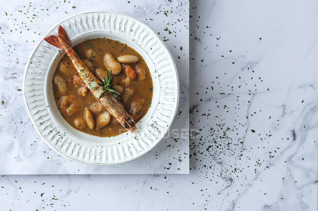 Сверху аппетитный кремовый суп с белой фасолью и лангустинами подается в миске и помещается на мраморный стол на кухне — стоковое фото