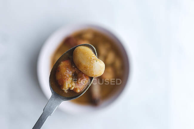 Top view spoon with saucy white beans over bowl with delicious dish with langoustines served on white table — Stock Photo