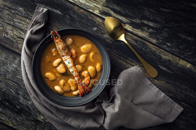 From above of appetizing cream soup with white beans and langoustines served in bowl and placed on wooden tabletop near napkin in kitchen — Stock Photo