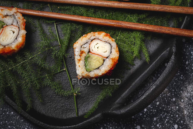 Zusammensetzung von köstlichen frischen verschiedenen Sushi und Bambusstäbchen, serviert auf schwarzer Platte auf kariertem Tuch — Stockfoto