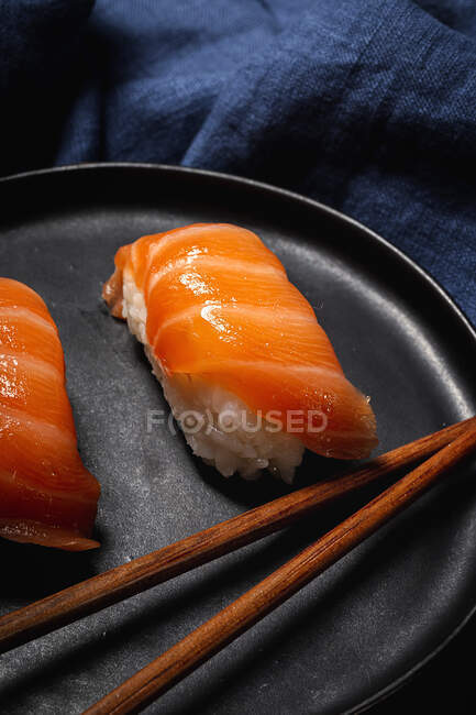 Zusammensetzung von köstlichem frischem Sushi und Bambusstäbchen, serviert auf schwarzem Teller auf kariertem Tuch — Stockfoto
