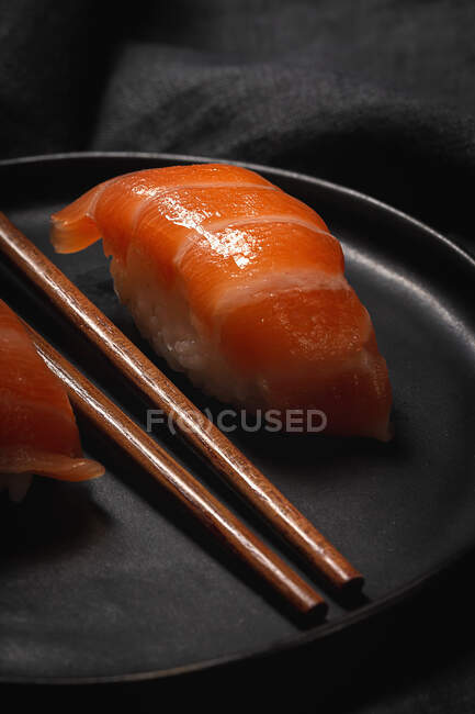 Верхний вид композиции вкусных свежих суши и бамбуковых палочек подается на черном блюде на клетчатой ткани — стоковое фото