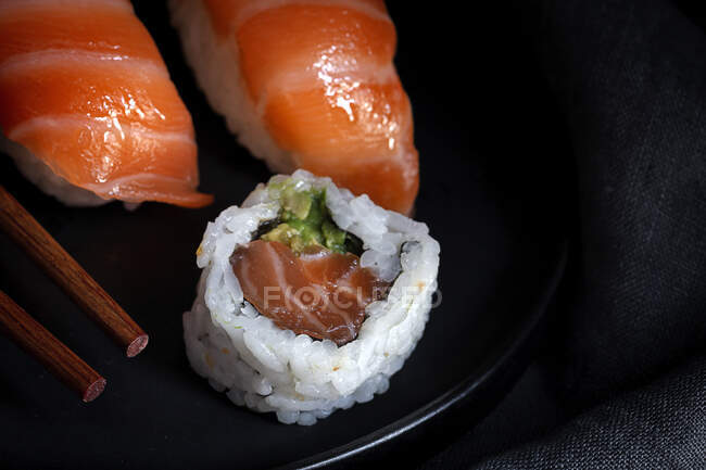 Zusammensetzung von köstlichem frischem Sushi und Bambusstäbchen, serviert auf schwarzem Teller auf kariertem Tuch — Stockfoto