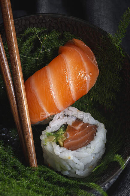 Sushi fresco saboroso servido em galhos de plantas verdes na placa preta com molho de soja na mesa de mármore perto de pauzinhos — Fotografia de Stock