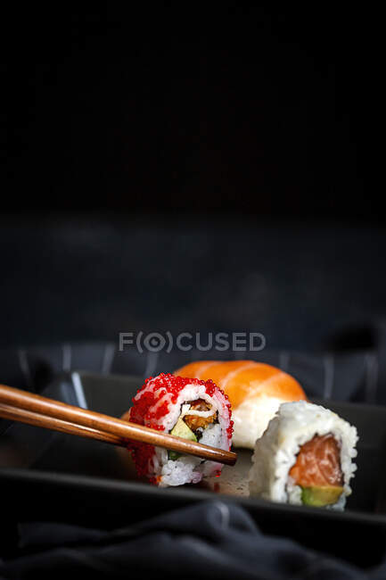 Vista dall'alto composizione di deliziosi sushi freschi vari e bacchette di bambù servite su piatto nero su un panno a scacchi — Foto stock