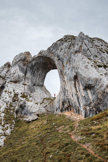 Distant traveler standing in large hole of rough rocky formation in Asturias Spain on cloudy day — Stock Photo