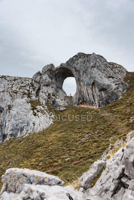 Viandante lontano in piedi in un grande buco di formazione rocciosa grezza nelle Asturie Spagna il giorno nuvoloso — Foto stock