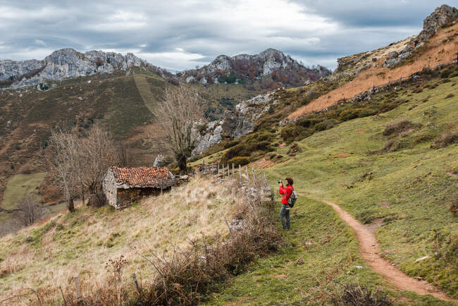 Seitenansicht gesichtsloser Reisender, der an einem bewölkten Tag in Asturien auf einem Feldweg am Grashang in großzügigem bergigem Gelände steht — Stockfoto
