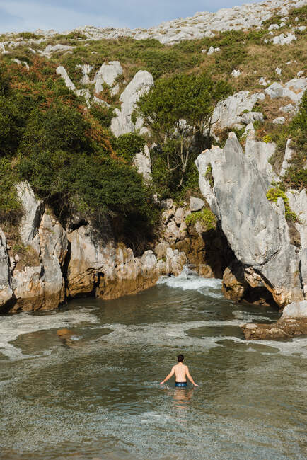 Anonymer schlanker Mann steht am ruhigen Binnenstrand des Sees, umgeben von schroffen Felsen in Asturien — Stockfoto