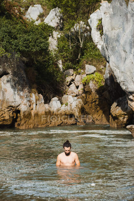 Undressed slim male standing on tranquil lake inland beach surrounded by rough rocky cliffs in Asturias — Stock Photo