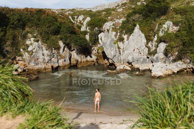 Rückansicht Unbekleideter schlanker Mann steht am ruhigen Binnenstrand des Sees, umgeben von rauen Felswänden in Asturien — Stockfoto