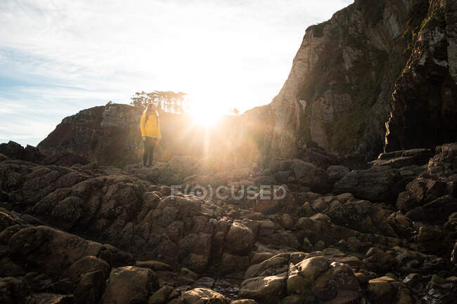 Ganzkörpergesichtslose Touristin in warmer Jacke steht auf einem steinigen, rauen Felshang gegen Sonnenstrahl und genießt die Aussicht auf das Hochland — Stockfoto