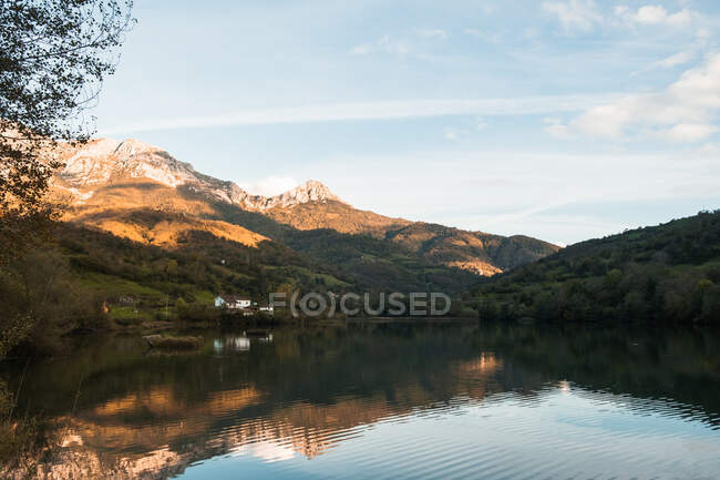 Picturesque scenery of peaceful rippling Reservoir Valdemurio on bottom of severe rocky mountains and lush green forest under clear blue sky — Stock Photo
