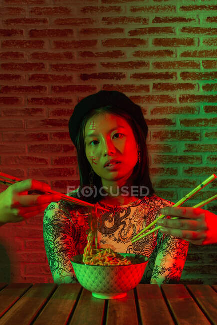 Crop anonymous people raising hands with chopsticks near amazed Asian woman with bowl with noodle — Stock Photo