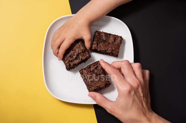 Hands picking pieces of fresh brownie on black and yellow background — Stock Photo
