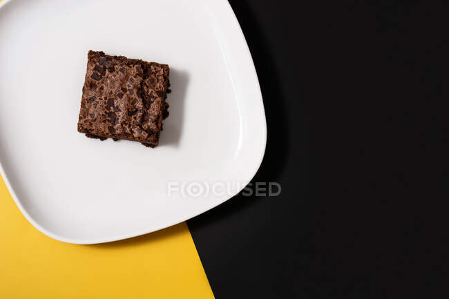 Piece of fresh brownie on black and yellow background — Stock Photo