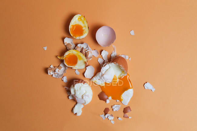 Top view of soft boiled chicken eggs and eggshell scattered on peach background in studio — Stock Photo