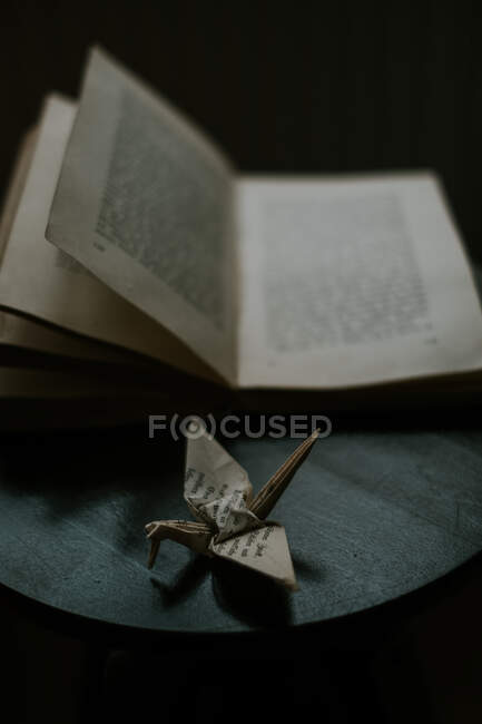 Бумажные оригами, изображающие птицу возле учебника на деревянном столе — стоковое фото