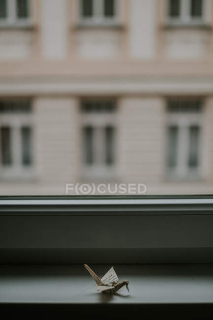 Handgeschöpftes Papier-Origami ähnlicher Kraniche gegen Fenster und Hausfassade in der Dämmerung auf verschwommenem Hintergrund — Stockfoto
