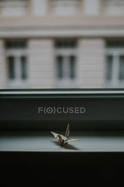 Origami de papel feito à mão representando guindastes semelhantes contra janela e fachada de casa no crepúsculo no fundo borrado — Fotografia de Stock