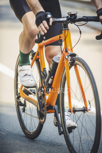 Crop ciclista irreconocible en pantalones cortos y zapatillas de deporte que monta bicicleta moderna en la soleada calle de verano - foto de stock