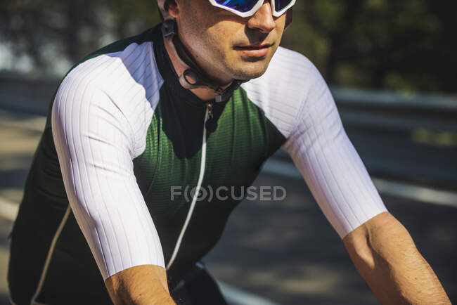 Crop of young sportsman in activewear and helmet riding bicycle on asphalt road on sunny day — Stock Photo