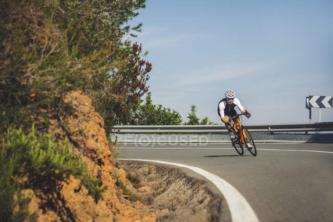 Cuerpo completo de joven deportista en ropa deportiva y casco a caballo bicicleta en carretera de asfalto en un día soleado - foto de stock