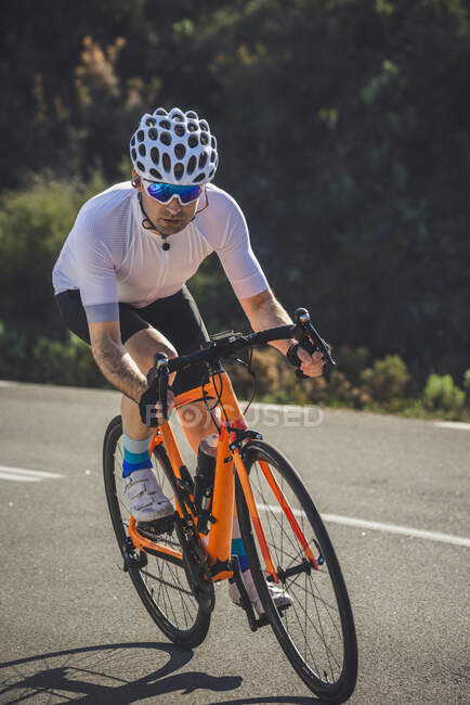 Cuerpo completo de joven deportista en ropa deportiva y casco a caballo bicicleta en carretera de asfalto en un día soleado - foto de stock