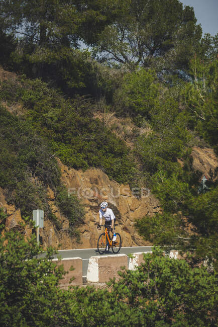 Full body of young sportsman in activewear and helmet riding bicycle on asphalt road on sunny day — Stock Photo