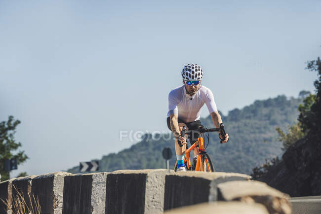 Повне тіло юного спортсмена в активному одязі і шоломі їде на велосипеді по асфальтовій дорозі в сонячний день — стокове фото