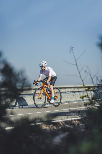 Full body of young sportsman in activewear and helmet riding bicycle on asphalt road on sunny day — Stock Photo