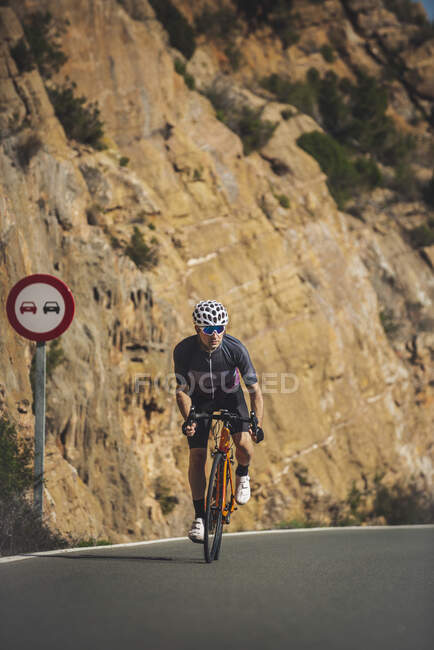 Corpo inteiro de jovem desportista em activewear e capacete andar de bicicleta na estrada de asfalto no dia ensolarado — Fotografia de Stock