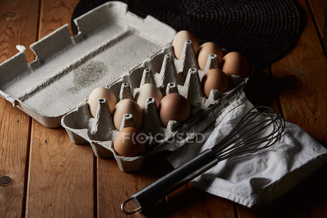 From above of container with eggs placed near whisk on napkin in kitchen — Stock Photo
