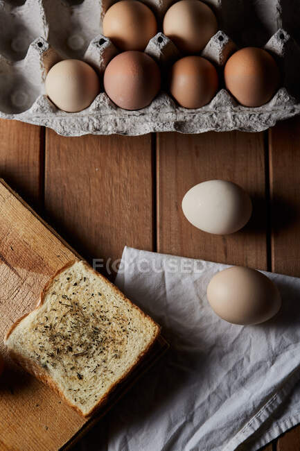 Blick von oben auf komponierte Eier und Brot auf dem Holztisch in der Küche zum Kochen des Frühstücks — Stockfoto
