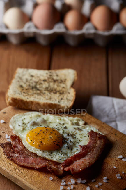 Сверху аппетитные жареные яйца подаются со свежим хлебом на деревянной доске — стоковое фото