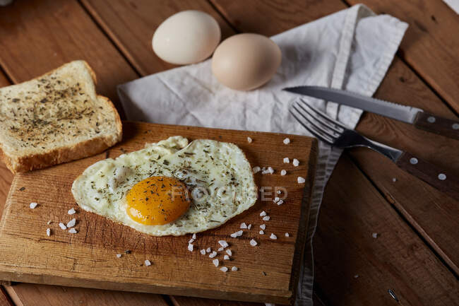 Сверху аппетитные жареные яйца подаются со свежим хлебом на деревянной доске — стоковое фото