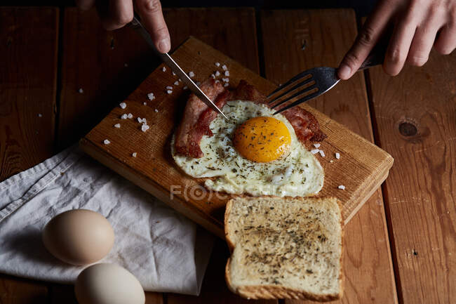 From above of crop anonymous person chopping roast eggs and bacon with knife and fork for breakfast — Stock Photo