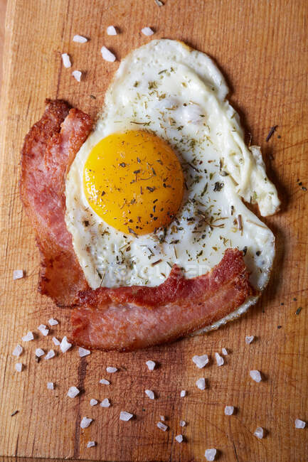 Top view of tasty homemade fried eggs with yolk and bacon seasoned with spices and salt — Stock Photo
