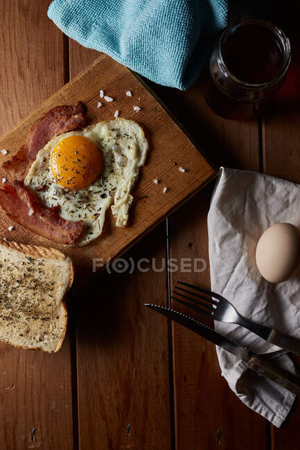 Top view of tasty homemade fried eggs with yolk and bacon seasoned with spices and salt — Stock Photo