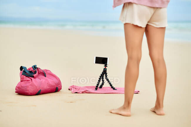 Recadré entraînement actif féminin voyageur méconnaissable sur la plage de sable et enregistrement vidéo sur téléphone mobile — Photo de stock