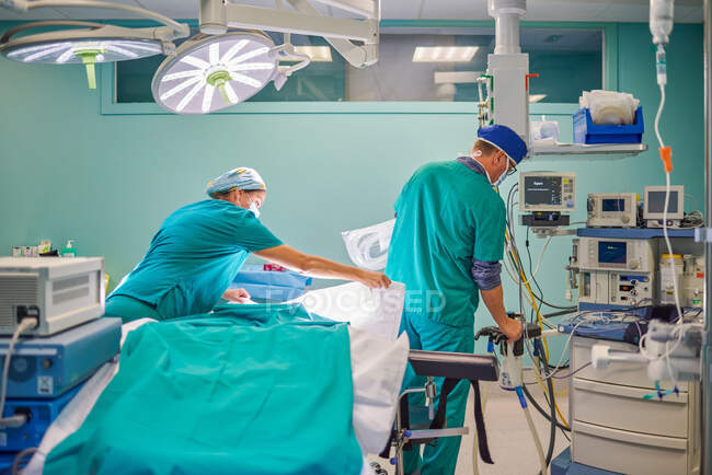 Back view of unrecognizable male and female medical assistants in uniforms preparing couch and devices in operating room for surgery in modern hospital — Stock Photo