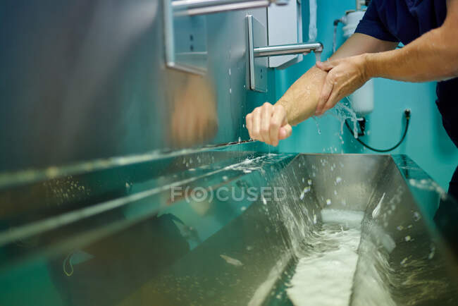 Crop medico maschio senza volto in uniforme medica lavarsi le mani sotto il rubinetto mentre si prepara per l'operazione in clinica moderna — Foto stock